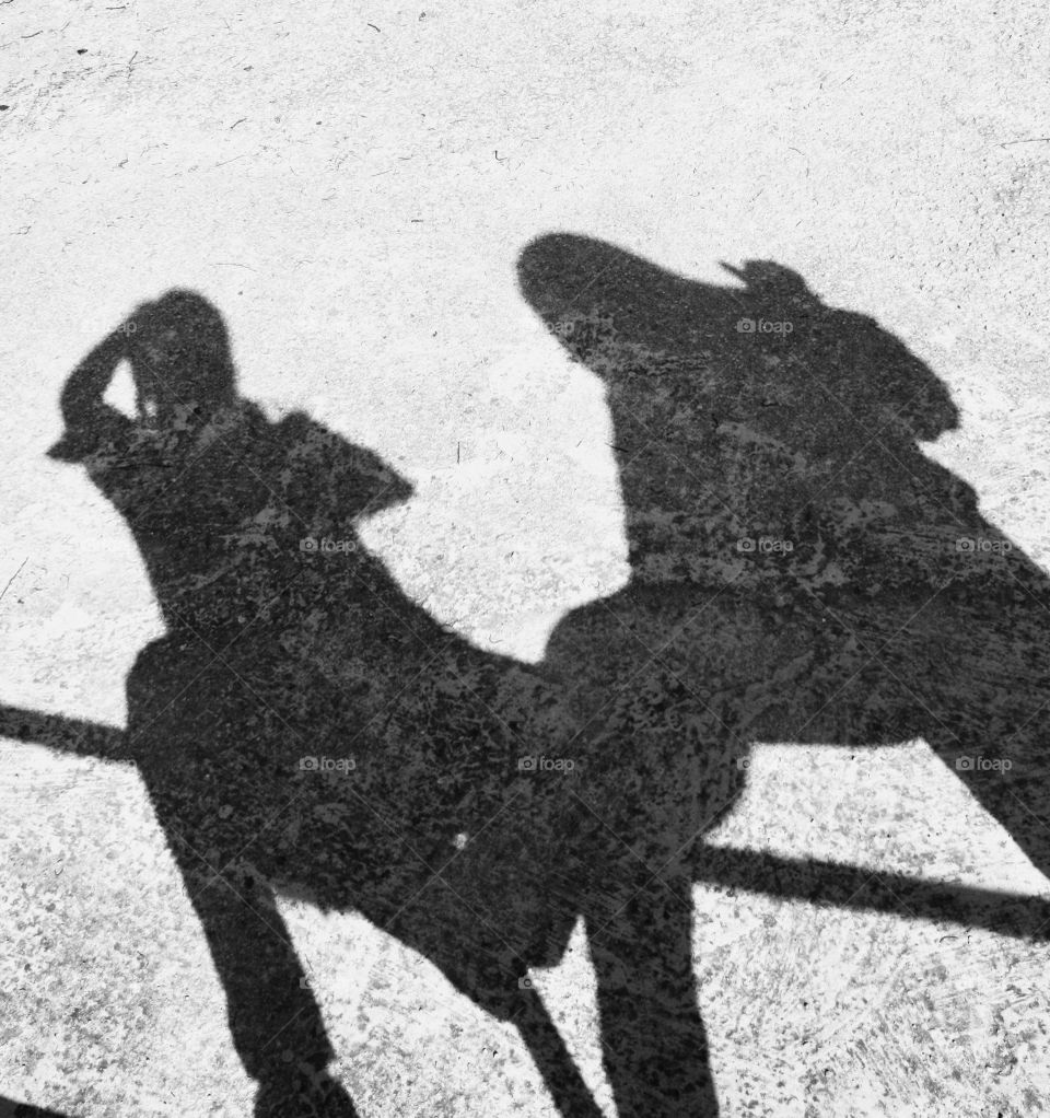 They are two shadows on the asphalt. There are two people in the shade. In the shade I go out taking the photo and my mother.