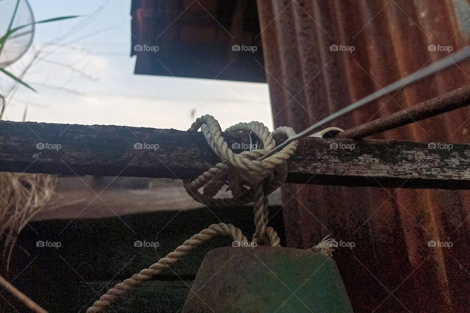 Close-up of a rope tied to an old, rusty wooden beam, against an equally rusty metal wall in the background