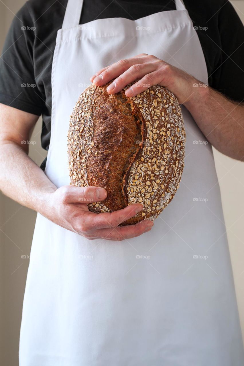 Close-up at bakers hands holding a loaf of sourdough bread in front of him.