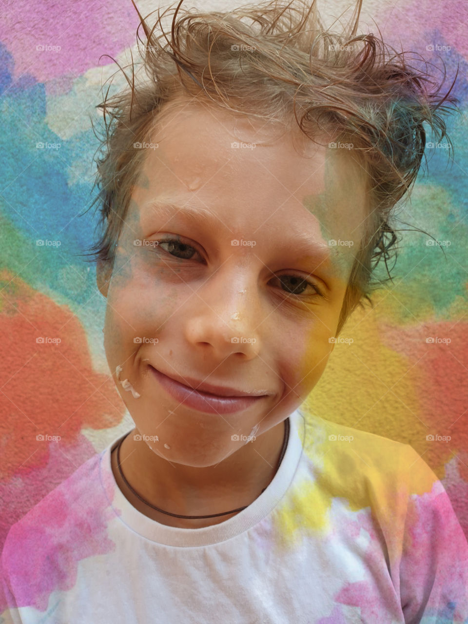 Selfie of a boy, a schoolboy after drawing, stained with paint with a dirty face, with tousled hair on the background of the wall and decorative watercolor smudges.  Children's creativity