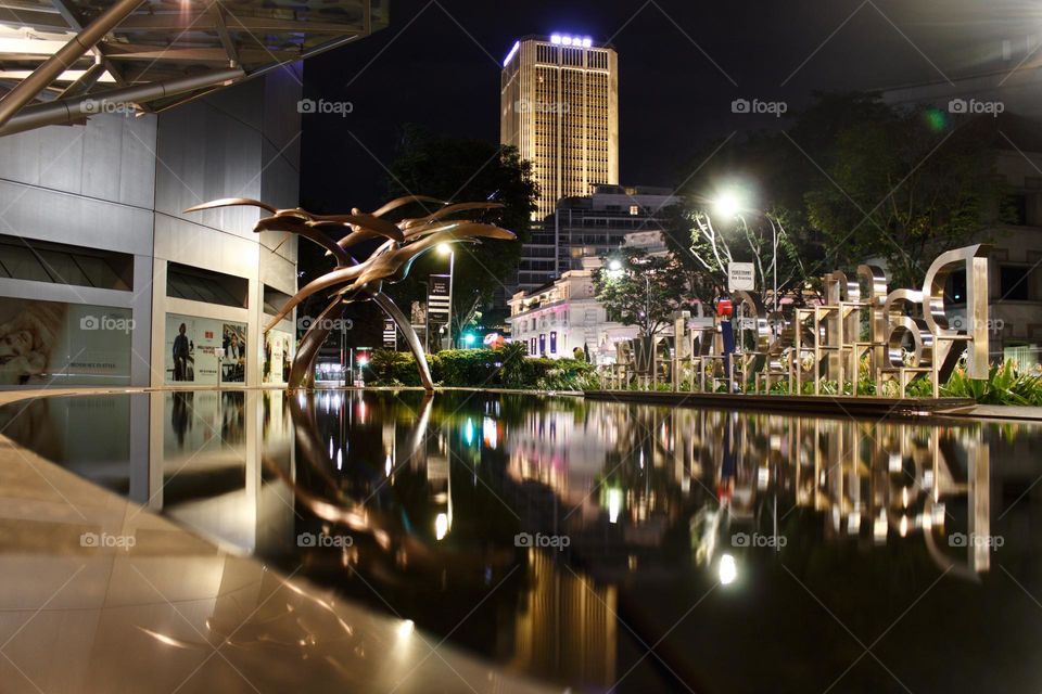 Reflection at night of tall building and night lights in a water fountain.