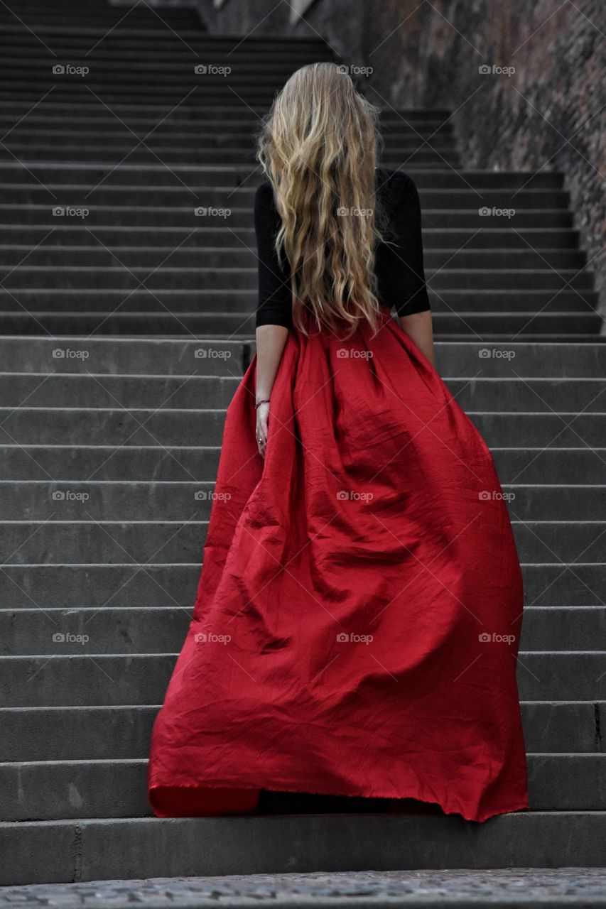 Blonde long hair woman in long red skirt standing on the stairs in old Prague