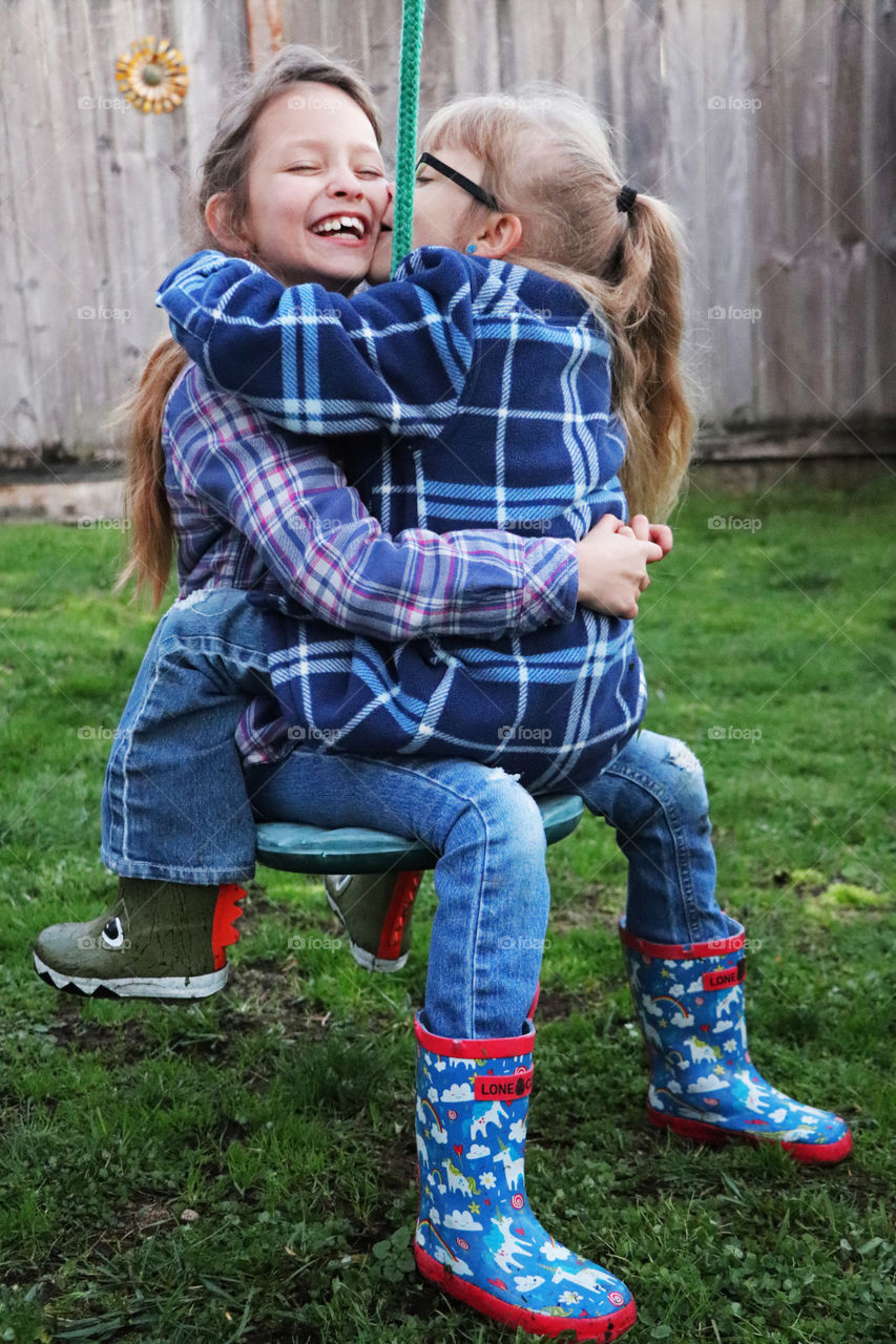 Sisters hugging each other on a swing