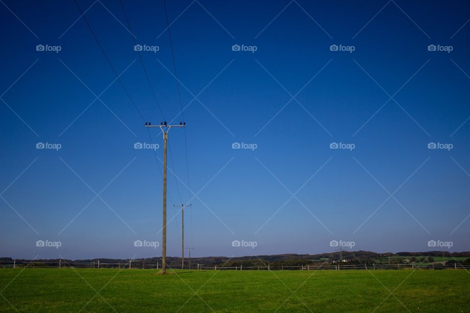 Power poles on grassy hill with blue sky