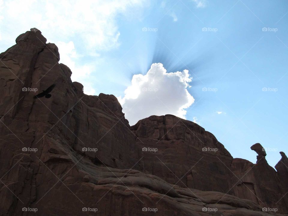 Sun behind cloud above rock formation. Bird flying