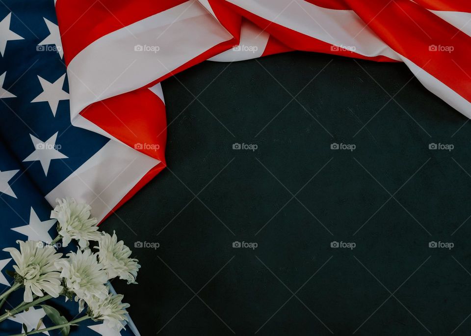 One American flag with white gerbera flowers lie on the left on a black background with copy space on the right, flat lay close up.