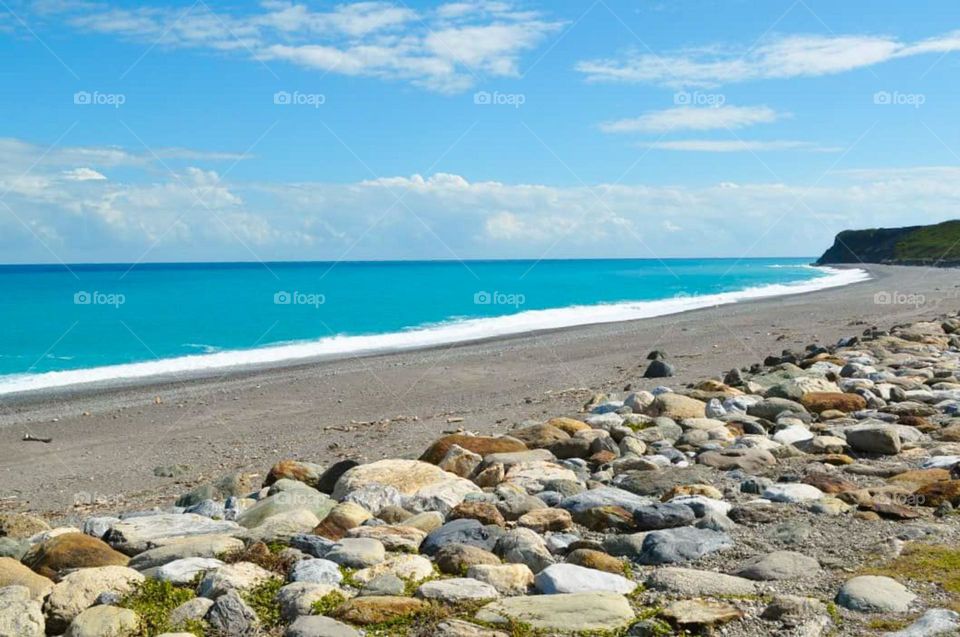 Portrait of a beautiful beach view with bright blue sea water, clear sky, and large rocks on the beach