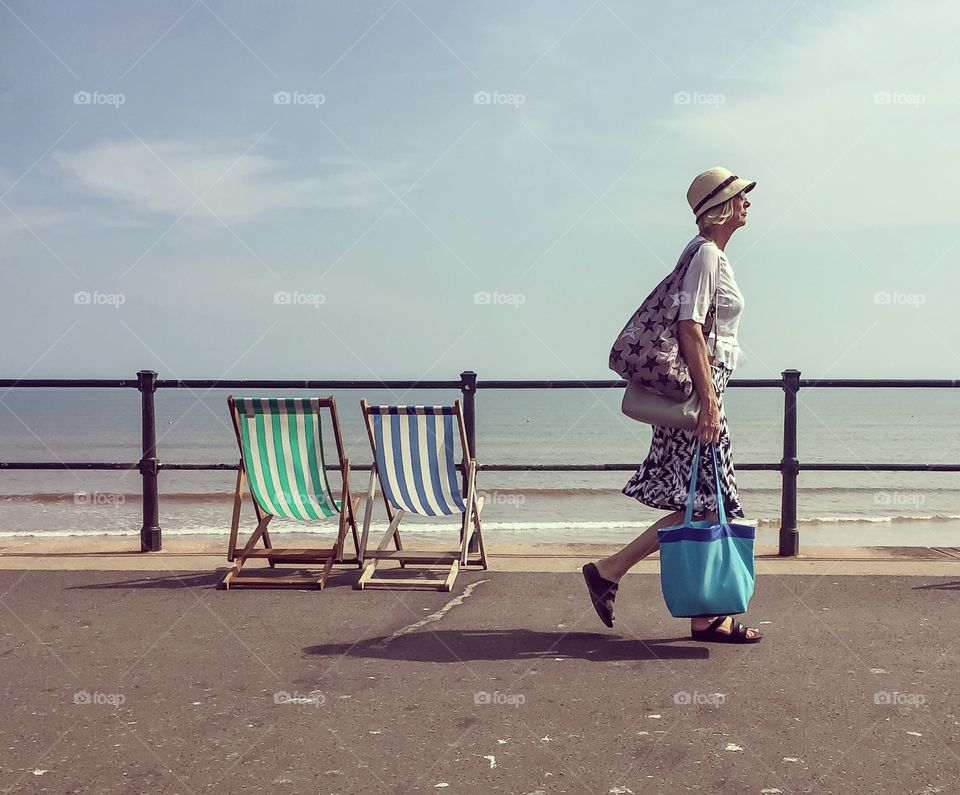 Senior woman walking on beach holding bag