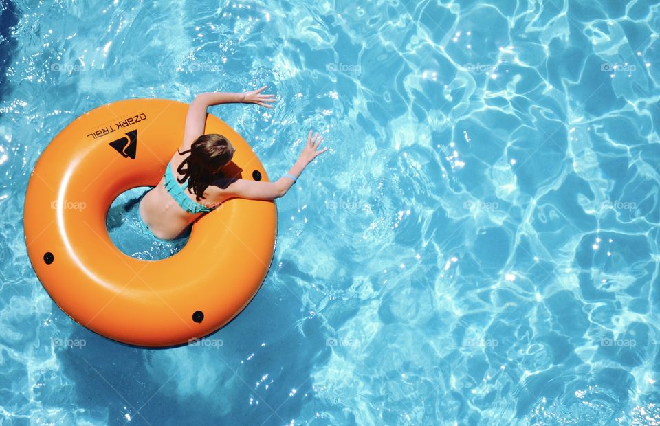 A young girl enjoys a relaxing float in a refreshing cool blue swimming pool. 