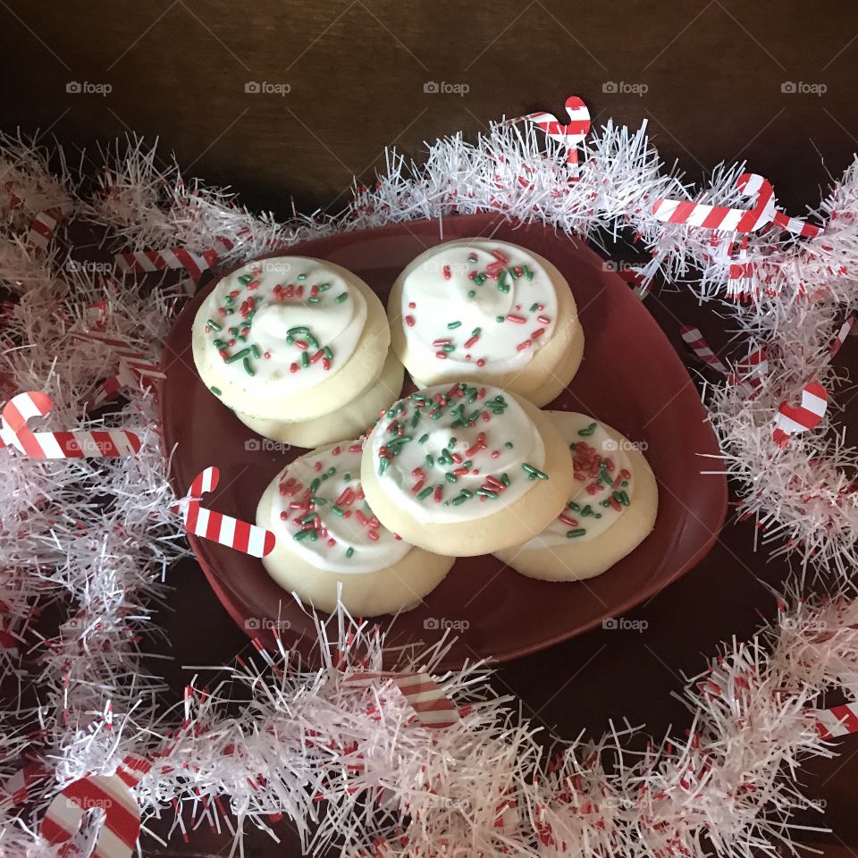 A beautiful plate of delicious Christmas sugar cookies with colorful red, green, and white sprinkles on a red plate in the kitchen.