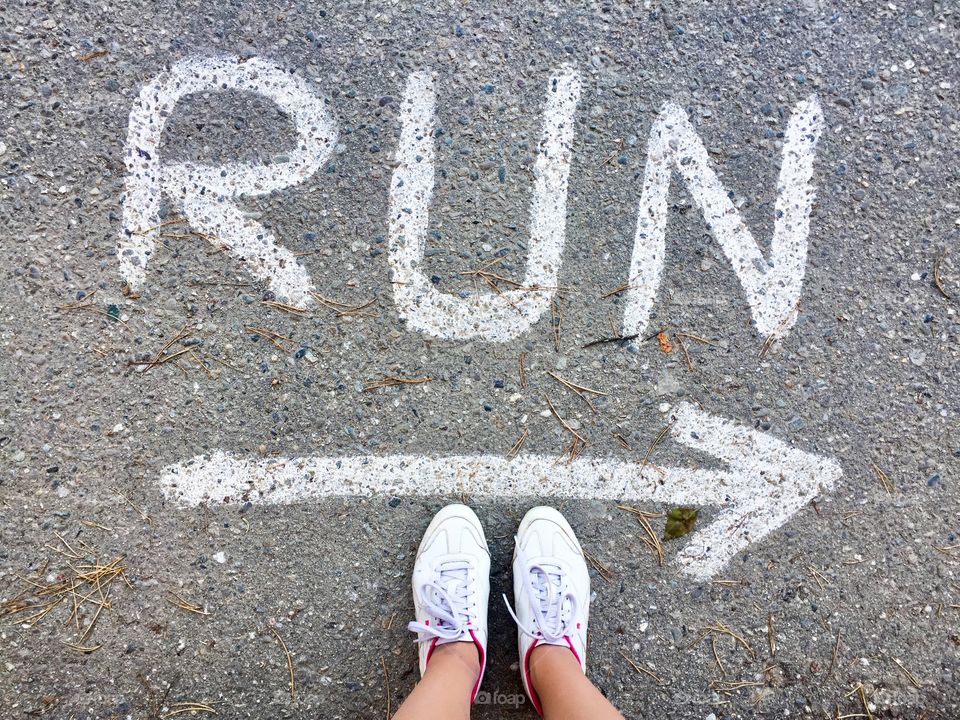 Top view of woman's feet wearing white and pink sneakers standing near run sign