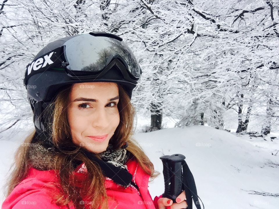 Selfie of pretty woman wearing uvex ski glasses and uvex ski with trees covered in snow in the background