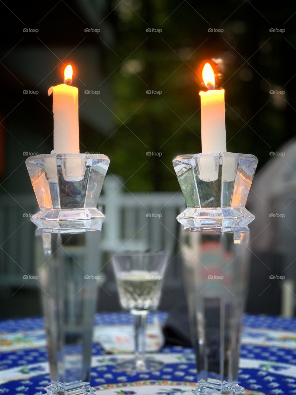 Two candle lighting in a glass candle holder. With wine glass at the center of it. At the terrace.