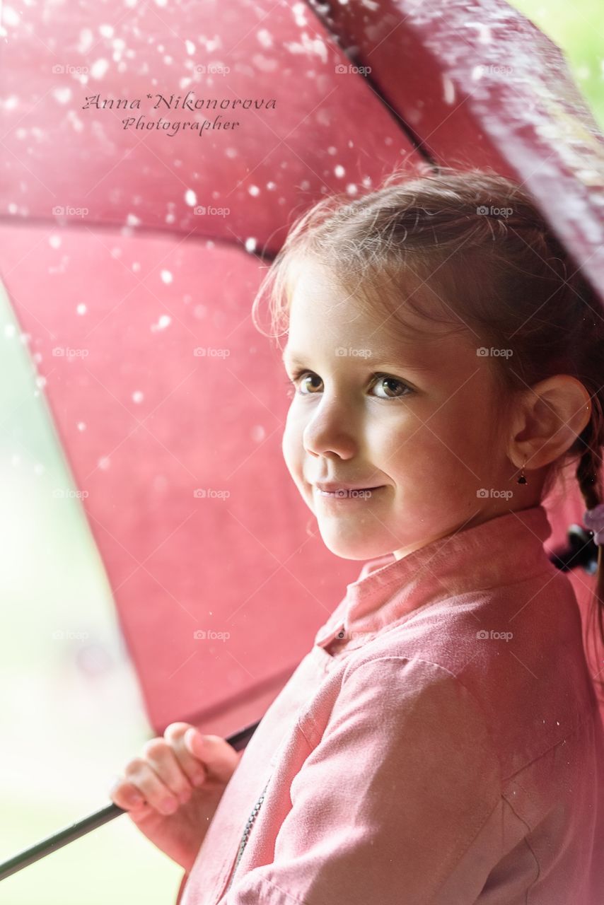 Portrait of a little girl under an umbrella in the rain waiting on the street close-up