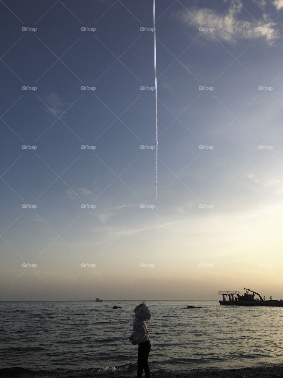 Little girl looks at the track of an airplane in the sky 