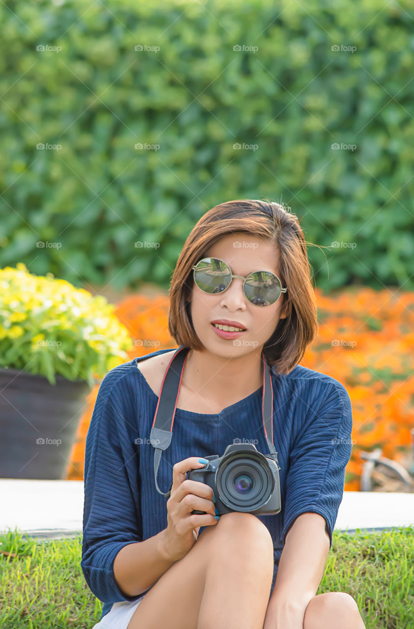 Hand woman holding the camera Background of trees and flowers