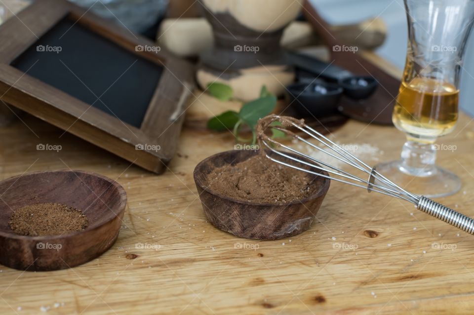 Weekly indulgence making facial moisturizer and facial scrub with honey, raw sugar, cocoa, mint, nutmeg, cinnamon. Preparation for beauty routine natural skincare on wooden prep table with measuring spoons and wire whisk 