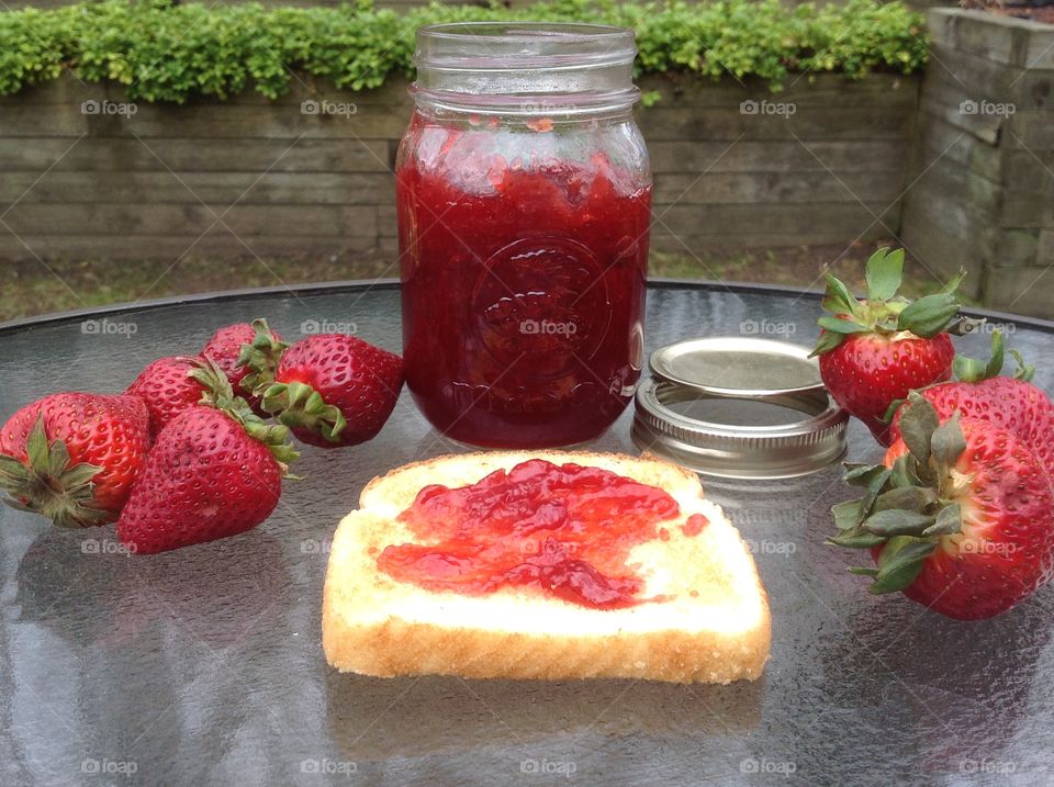 Homemade strawberry jam in a jar with a slice of toast.