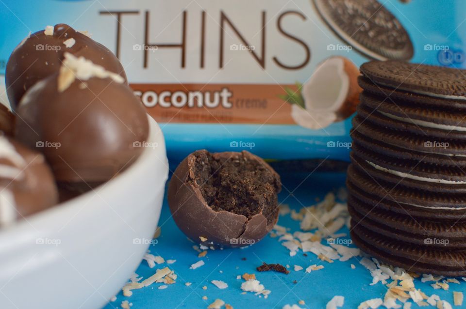 A stack of coconut Oreo thin cookies on a blue background with coconut shreds with truffles 
