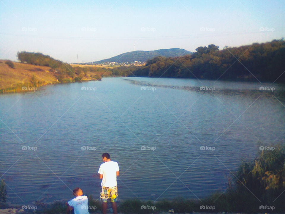 Down by the lake. Two friends sharing interesting stories while sun slowly goes down on a hot summer day. 