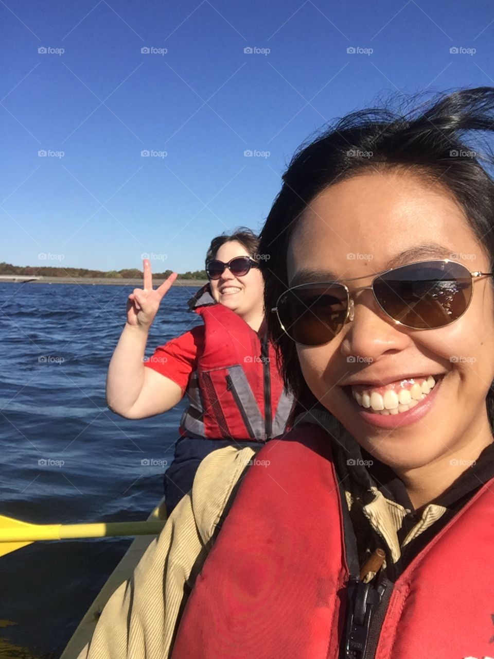 Two happy female travelling on boat showing peace sign