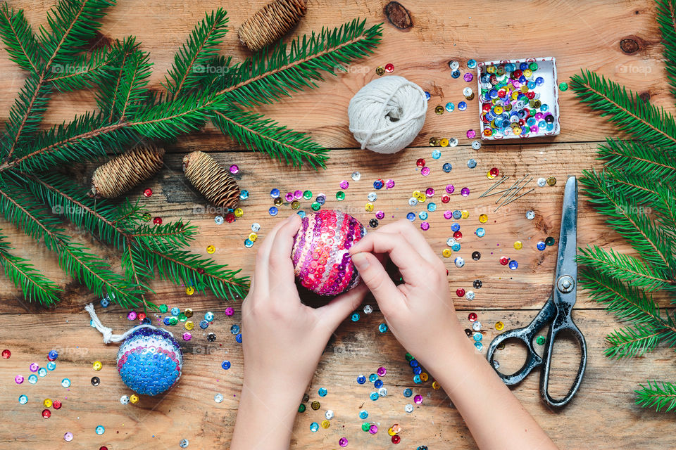 Girl making Christmas decoration by pinning the sequins onto the ball