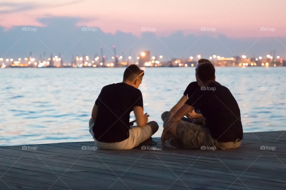 Teenagers Sitting At The Dock Talking And Enjoying The Night View
