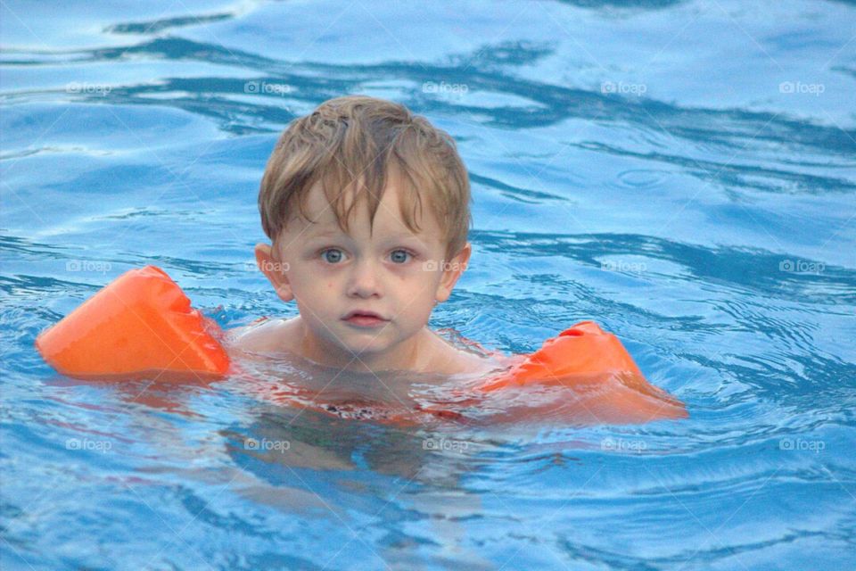 Adorable little boy swimming in the crystal blue water of a pool. 