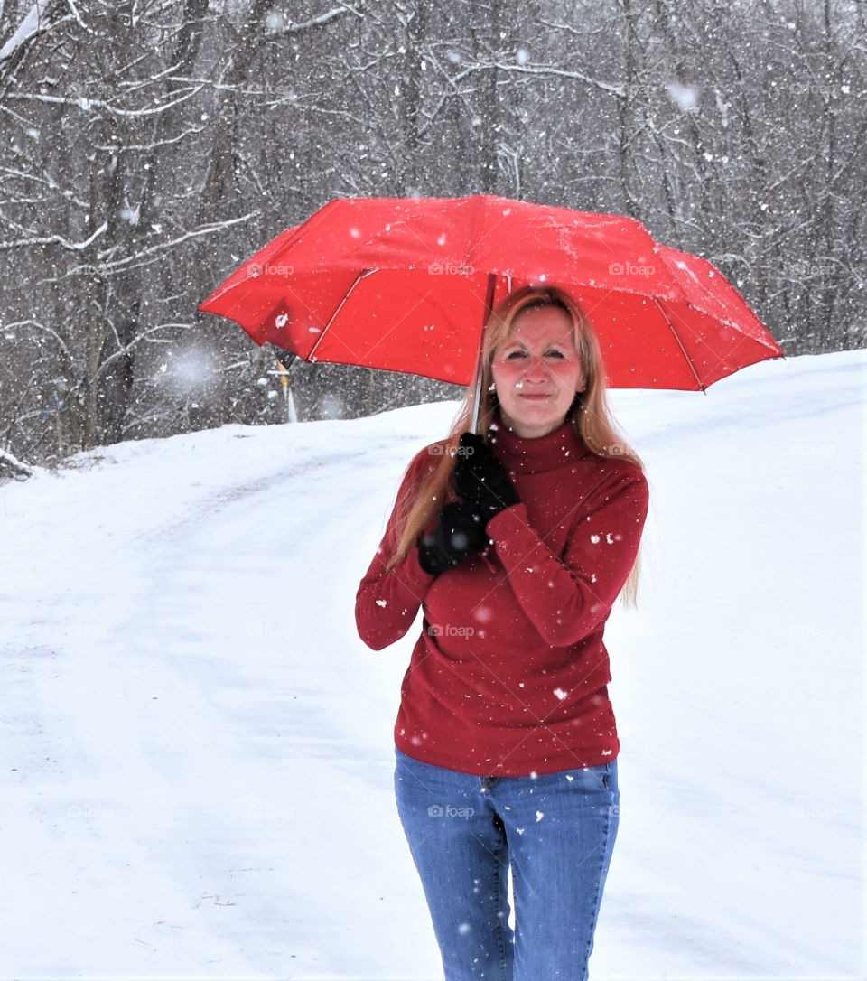 Woman with long blonde hair holding a red Totes umbrella during a snow storm 