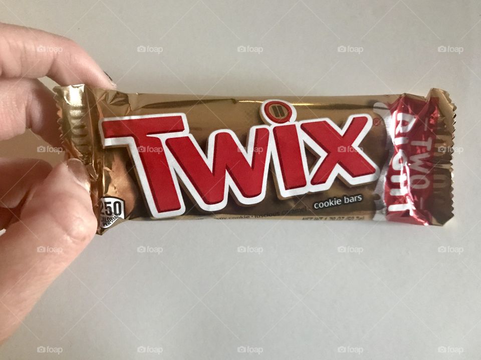 Twix caramel and chocolate candy bar being held by a woman’s hand against a white background. 
