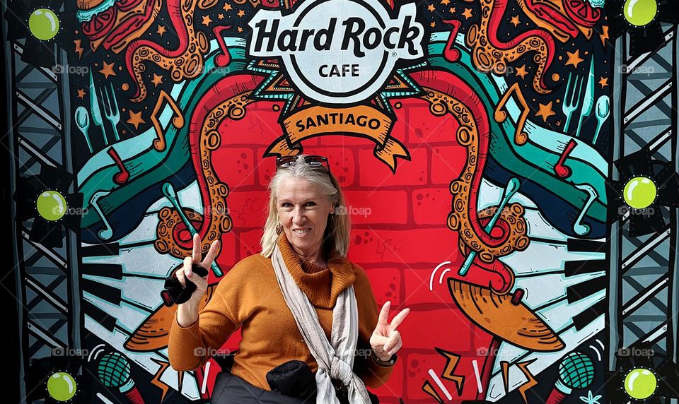 Pretty blonde woman smiling and showing peace sign in front of Hard Rock Cafe Santiago.