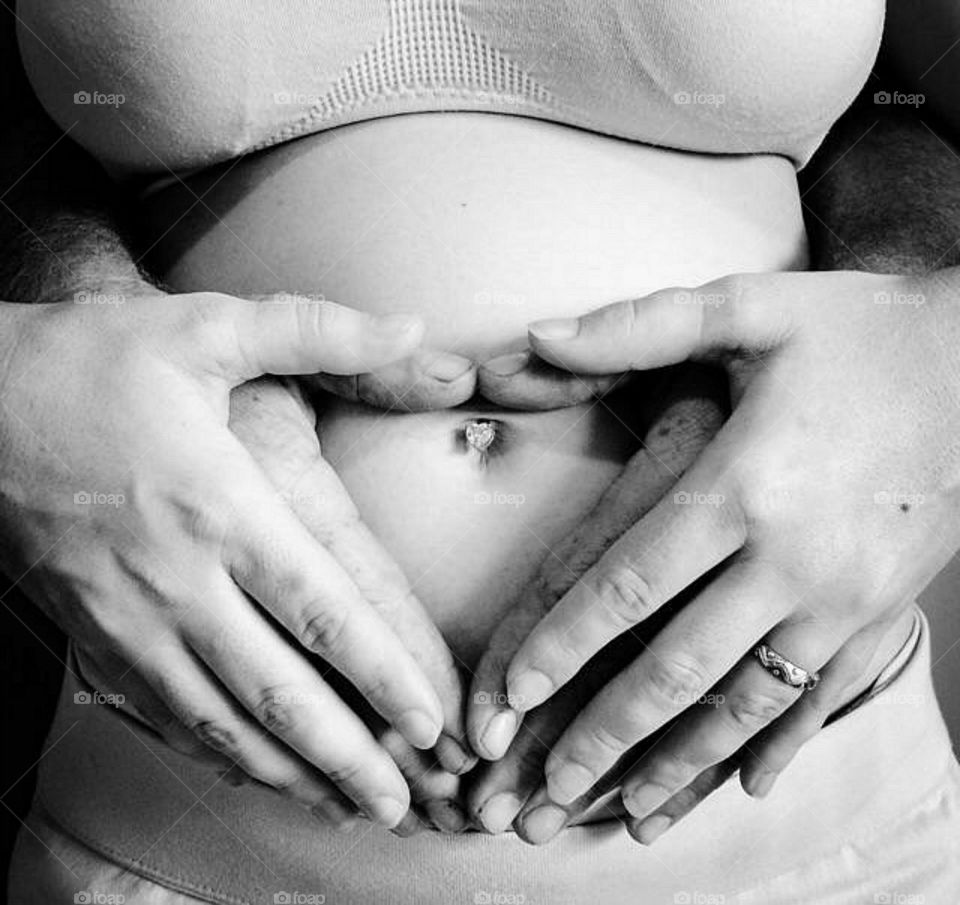 Husband and wife's heart shaped hands on pregnant belly