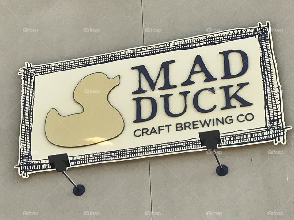 A large sign on the building with a shape of a duck representing the eatery. One would go mad like a duck after eating there.