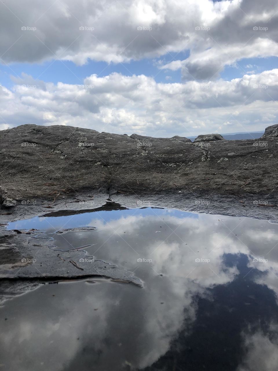 Rain puddle reflecting the sky. On the edge of a cliff it looks like a mountain and lake