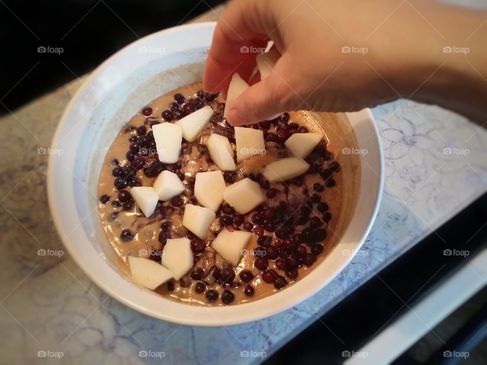 Woman's hand placing pears in an unbaked blueberry pear old fashioned cobbler getting ready to bake