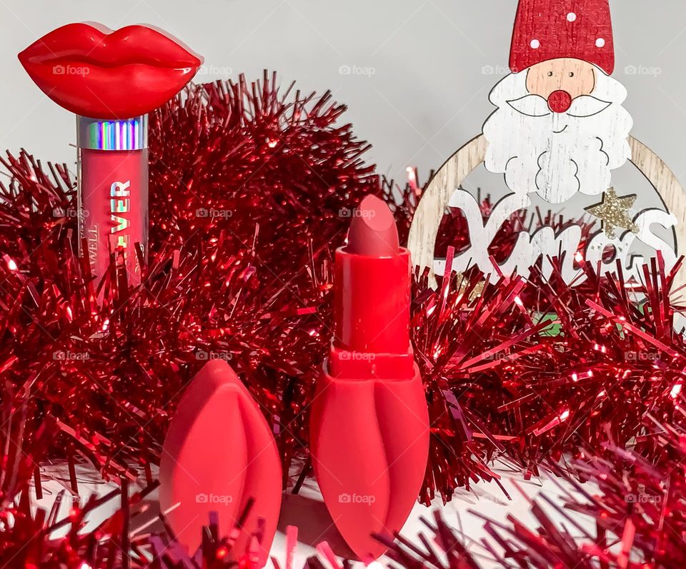 Red lipstick and lipgloss in lip shaped containers with a red christmasy tinsel background 