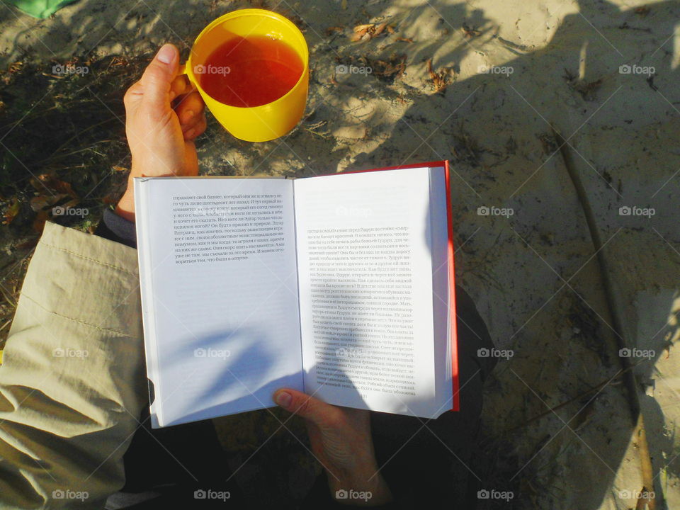 the girl is reading a book and is having tea in the open air