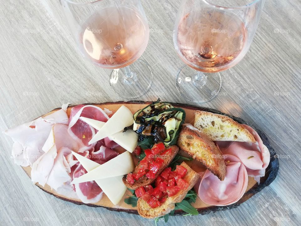 Chopping board with cheeses and cured meats and glasses of rosé wine photographed from above