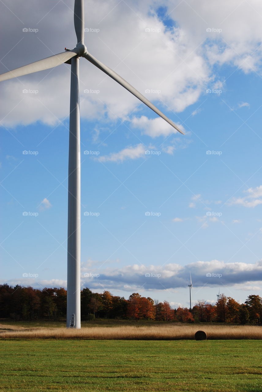 Windmill standing in farm hay field in autumn with blue sky and clouds wind power landscape