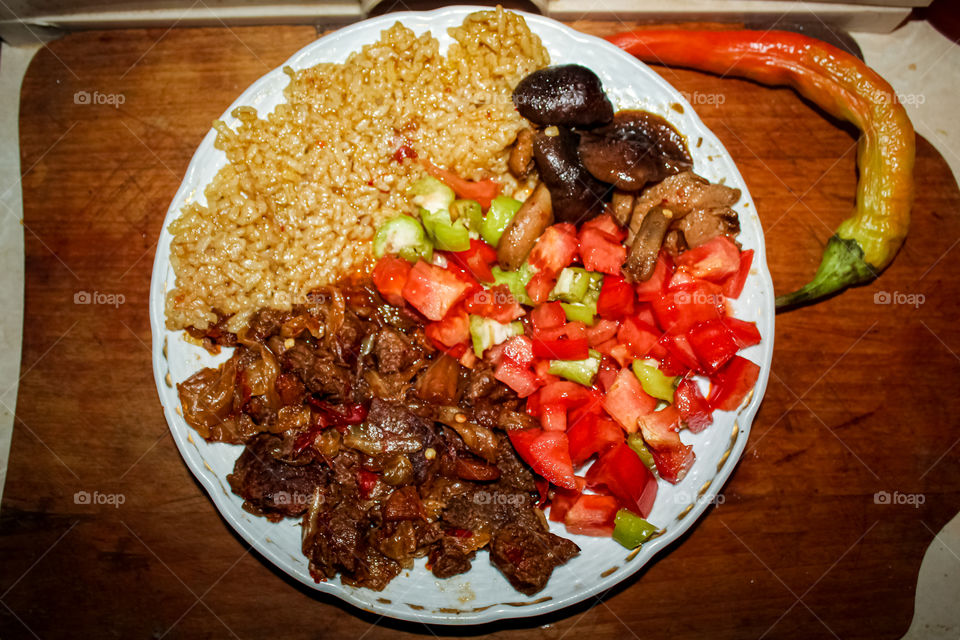 Served on a plate: chopped beef prepared in soy sauce, chopped tomato with chopped green peppers, rice with soy sauce, garnish with green red pepper, shoot date 10.11.2021.