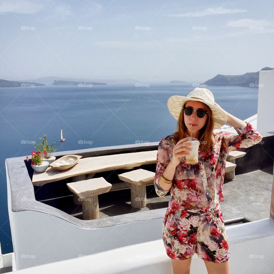 A tourist in a floral jumpsuit pauses to sip an iced coffee on a beautiful island in Greece 