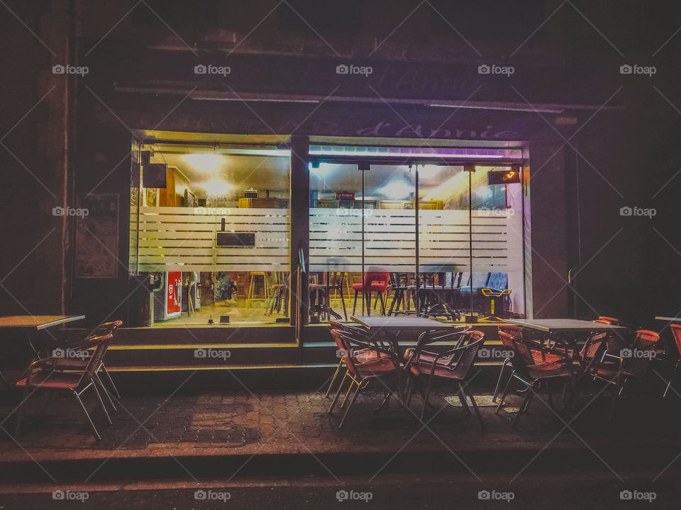 A quiet French cafe bar, gently illuminates the empty street outside