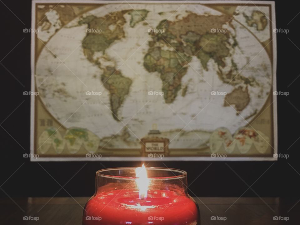 Fall scented, red candle burning on a wooden table in front of a vintage, rustic looking map 