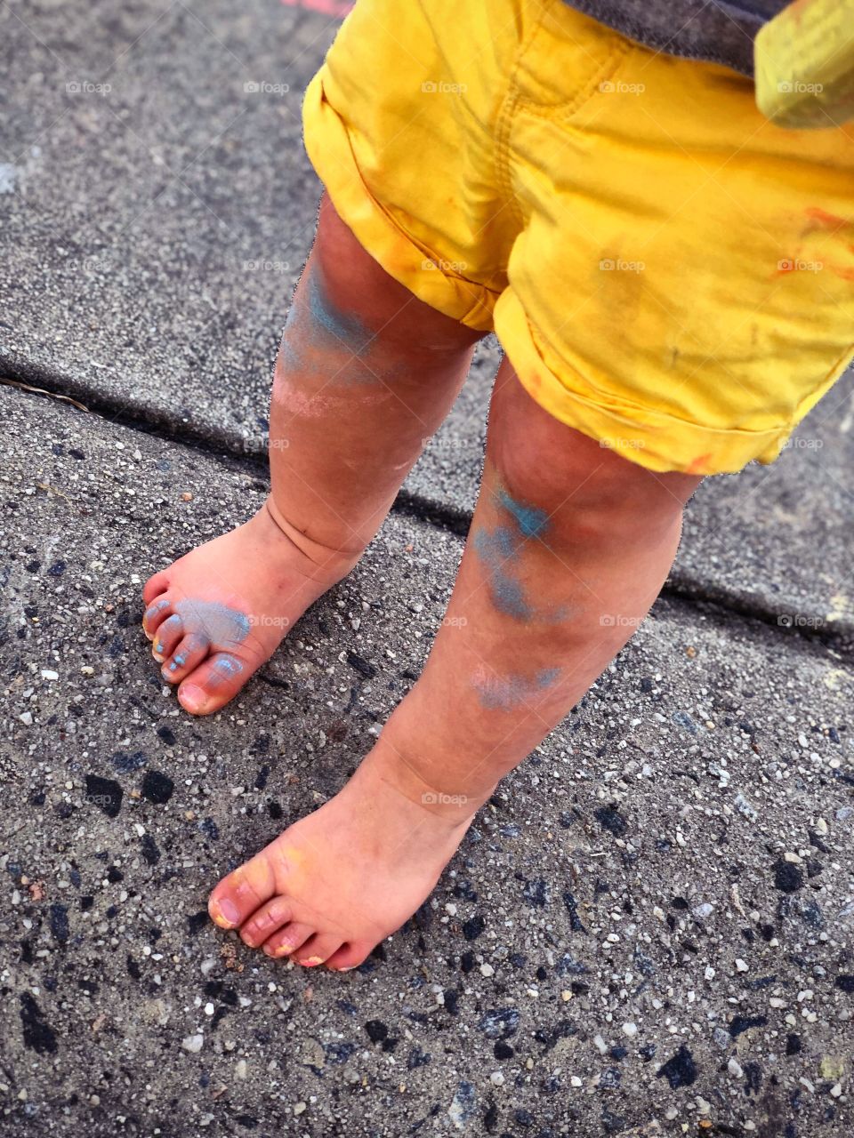 Toddlers feet, dirty with sidewalk chalk while coloring the driveway outside.