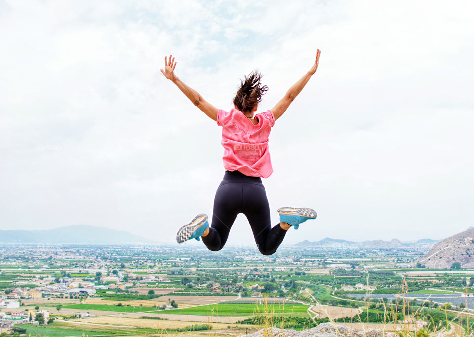 Rear view of young woman at mountain top jumping in the air