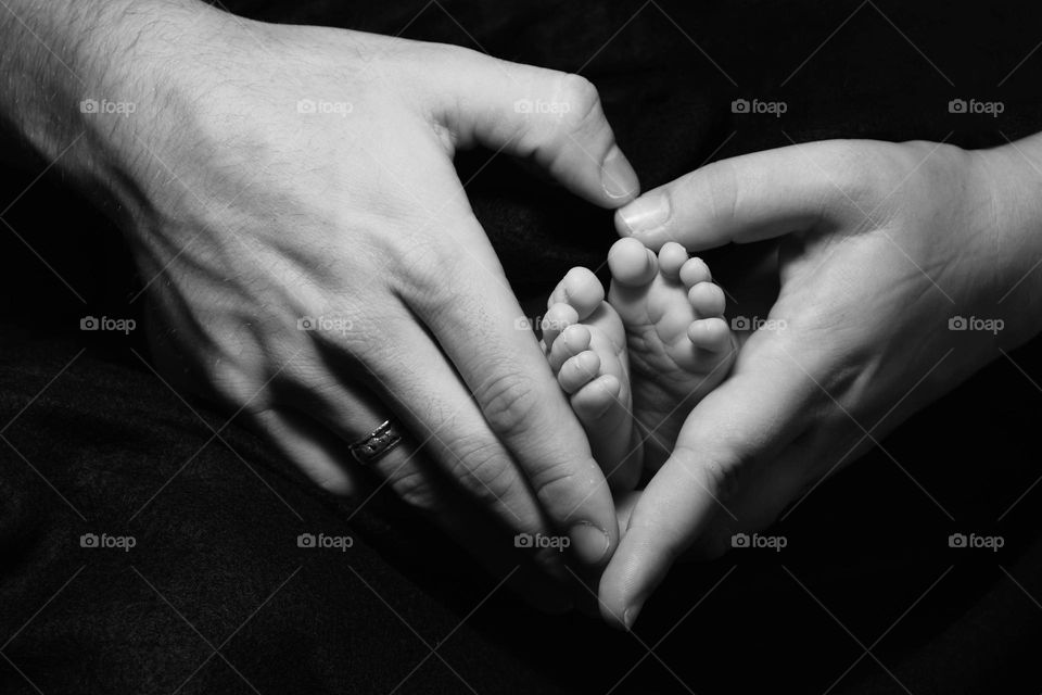 Father and mother’s hands shaped like a heart holding their baby’s feet