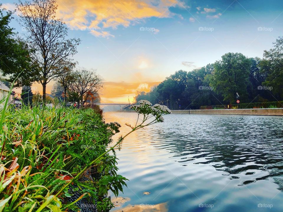 Soft sunrise over a Countryside landscape reflected in the water of the river as seen from the Grassy riverside.