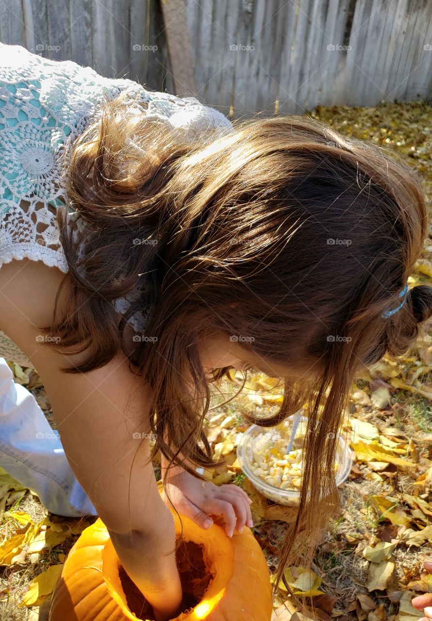 child gutting and carving a big orange pumkin outside surrounded by autumn leaves
