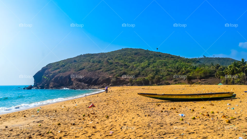 Fishing boats on beautiful sea shore at sunrise or sunset. Wild Empty Tropical beach, blue sky, yellow sand, sunlight reflections taken in background landscape style. Travel vacation destination.