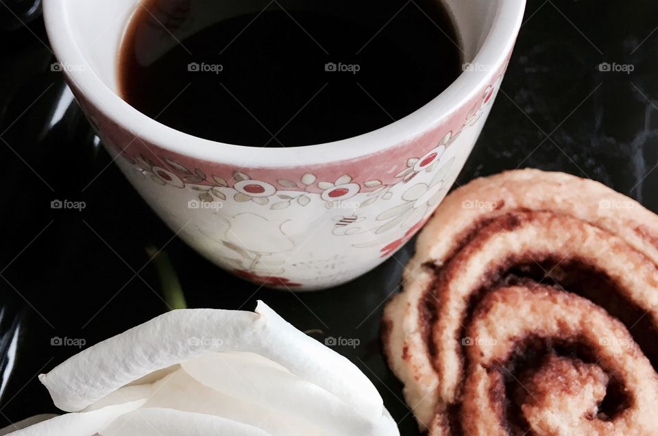 Coffee and breakfast in bed. Black Coffee, cinnamon roll, white rose on black tray. 